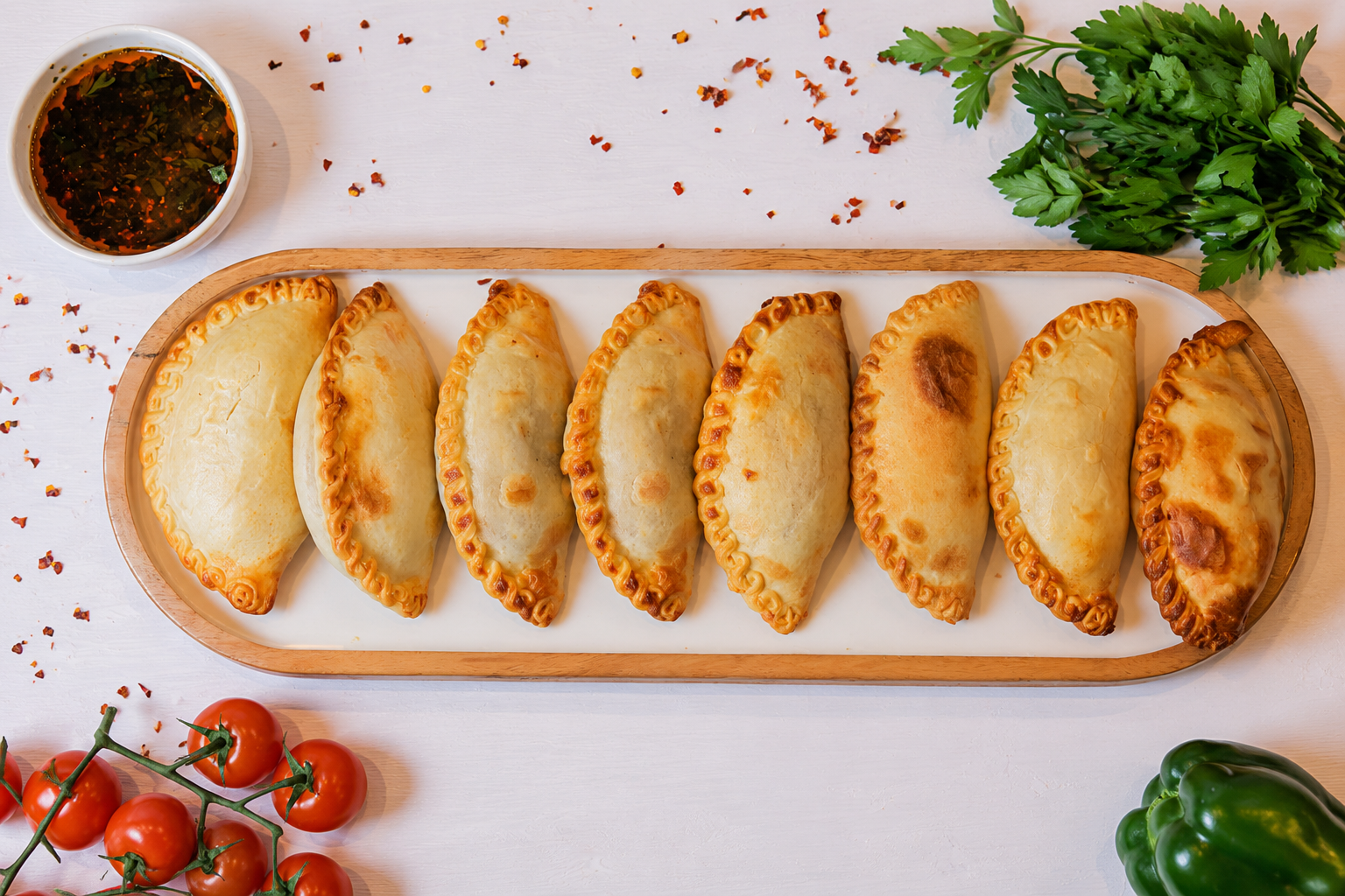 Golden Argentine empanadas made with love and dedication, served on a tray with chimichurri, herbs and fresh vegetables